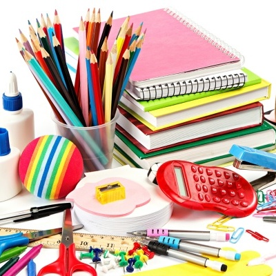 Materiais escolares diversos incluindo lápis de cor, calculadora vermelha, cadernos, cola e acessórios sobre fundo branco.