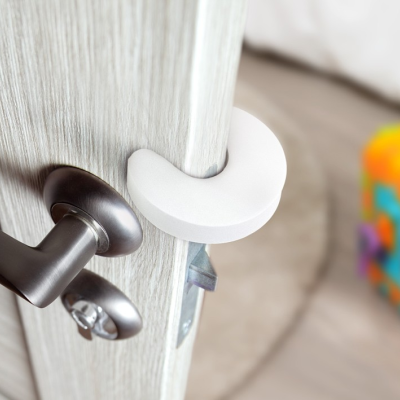 Protetor branco colocado na borda de porta de madeira clara com maçaneta metálica escura