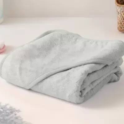 Toalha cinzenta dobrada sobre superfície branca com escova e frasco ao fundo