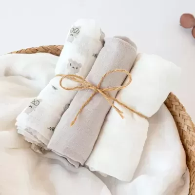 Três panos de musselina enrolados com padrões e cores neutras num cesto de palha