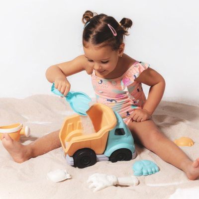 Criança a brincar na areia com camião de brinquedo e vários brinquedos de areia coloridos