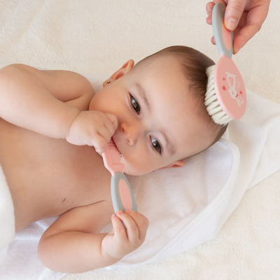 Bebé deitado com pente e escova para cabelo cor-de-rosa e cinza