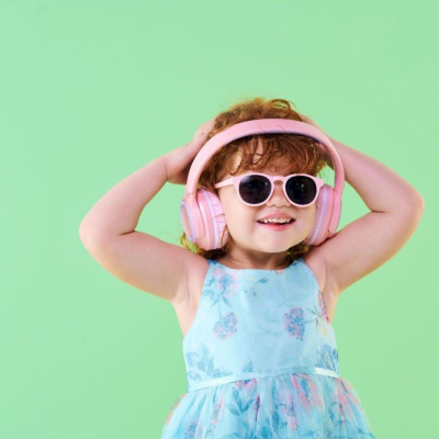 Criança com vestido azul claro e auscultadores rosa num fundo verde claro