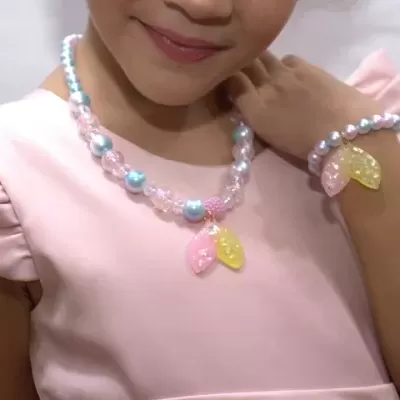 Colar e pulseira de contas coloridas com pendentes de folhas usados por criança com blusa rosa