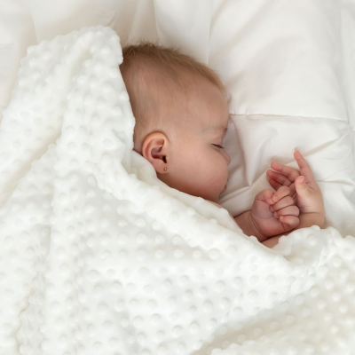 Bebé adormecido com uma manta branca texturizada em cama branca
