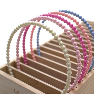 Cinco tiaras finas com pérolas falsas de cores diferentes numa caixa de madeira