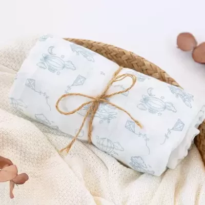 Fralda branca com padrão azul claro em cesto de palha com tecido branco e folhas secas ao lado