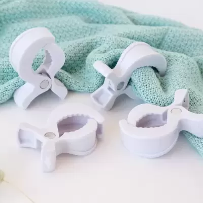 Quatro pregadores brancos de plástico com interior serrilhado sobre superfície branca e tecido azul claro