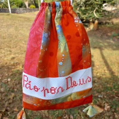 Saco colorido com cordão, padrão em laranja e vermelho e inscrição 