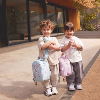 Duas crianças ao ar livre com mochilas azul clara e rosa claro e roupa casual