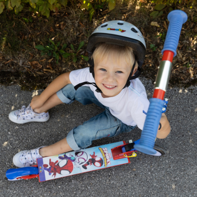 Criança com capacete e patinete do Homem-Aranha sentada no chão de alcatrão