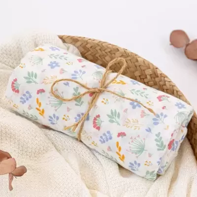 Manta enrolada com padrão floral amarrada com cordão numa cesta de vime
