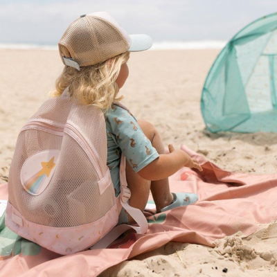 Criança na praia com mochila rosa e bege, boné e tapete cor de rosa