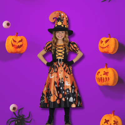 Menina vestida de bruxa em roupa de Halloween laranja e preta com chapéu pontudo, rodeada por abóboras e olhos de plástico