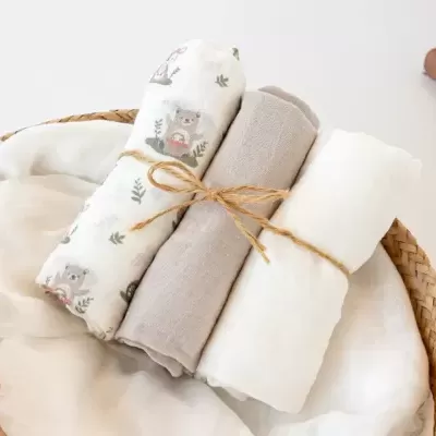 Três fraldas de algodão branco e cinzento com estampa de ursinhos, amarradas, em panier de vime sobre fundo branco