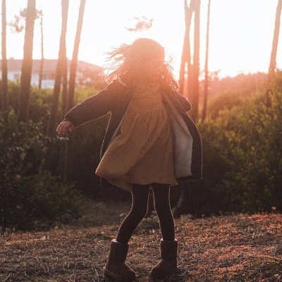 Criança de vestido bege e casaco preto a girar ao ar livre ao pôr do sol
