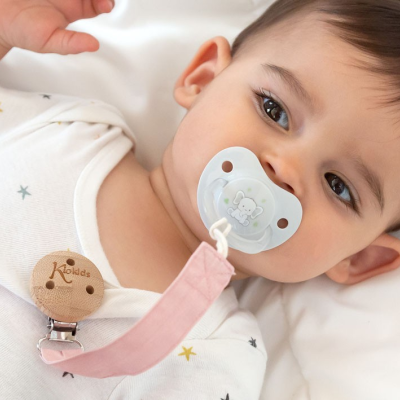 Bebé com chupeta transparente e clip de madeira em body branco com estrelas coloridas