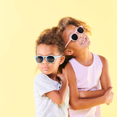 Dois miúdos com óculos de sol coloridos e roupa casual em fundo amarelo
