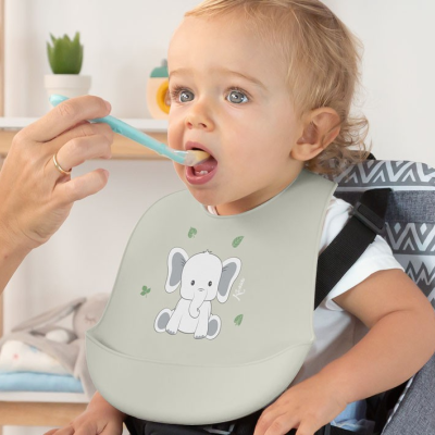 Criança com babete de silicone cinza claro com elefante, sentada em cadeira de alimentação.