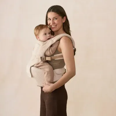Mochila porta-bebé bege acolchoada com bebé e mulher em fundo neutro claro