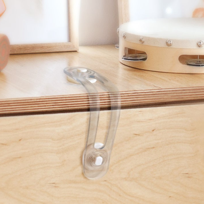 Trava de segurança transparente num móvel de madeira clara com pandeiro branco ao fundo.