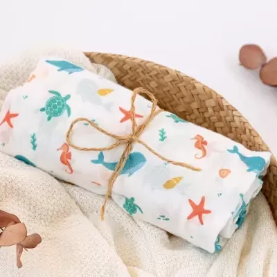 Fralda ou manta infantil com estampas marinhas coloridas, amarrada com cordão de ráfia numa cesta de vime