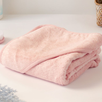 Toalha de banho cor-de-rosa dobrada em superfície branca com escova e frasco ao lado.