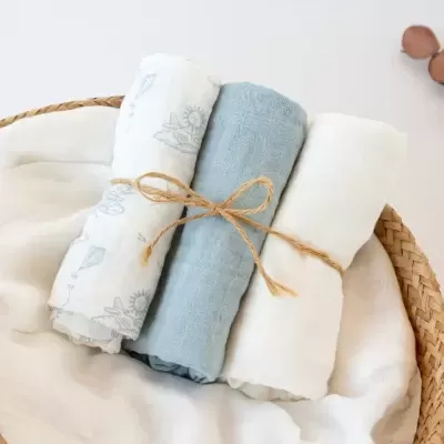 Três panos de tecido fino enrolados e amarrados com corda rústica em cesta de vime