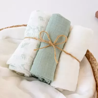 Conjunto de três panos enrolados em branco e verde com corda dentro de cesto de vime