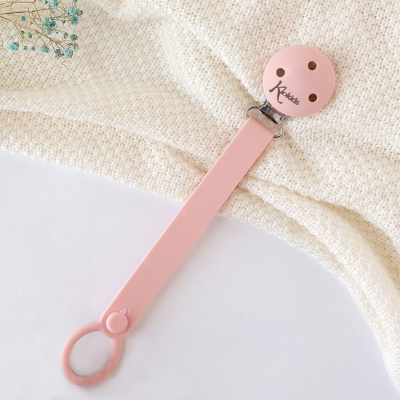 Prendedor de chupeta rosa com fecho metálico sobre tecido branco texturizado