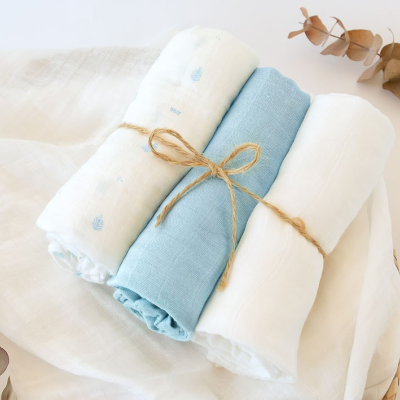 Três panos de tecido enrolados, dois brancos e um azul, com corda a amarrar e folhas secas ao lado