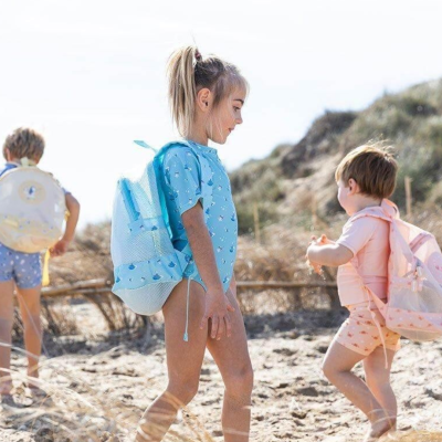 Crianças na praia com mochilas azuis, rosa e bege com padrões.