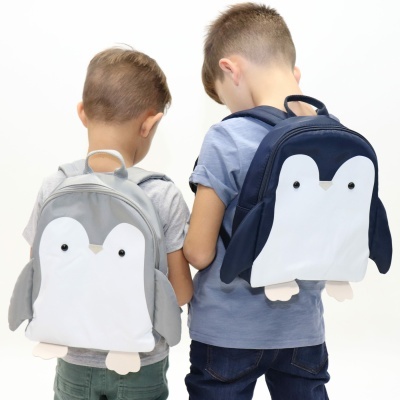 Duas crianças de costas com mochilas em forma de pinguim cinzenta e azul escura.