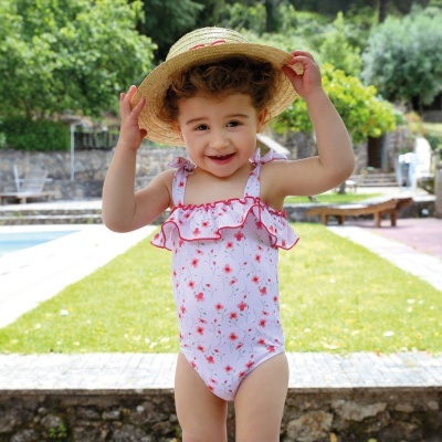 Menina com fato de banho branco com flores vermelhas e chapéu de palha num jardim com piscina