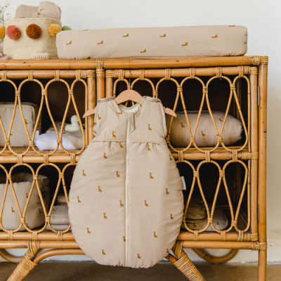 Móvel em rattan natural com acessórios de bebé em tecido bege com pequenos desenhos castanhos