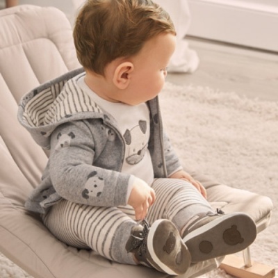 Bebé vestido de cinza com capuz, sentado numa cadeira bege acolchoada