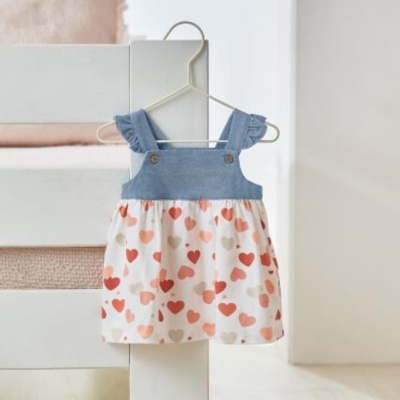 Vestido de bebé azul e branco com corações pendurado num cabide branco