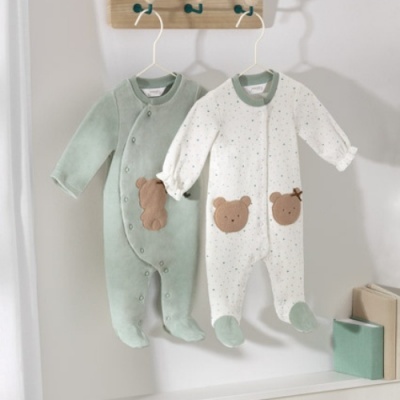 Dois macacões de bebé em verde e branco com ursinhos, pendurados em cabides.