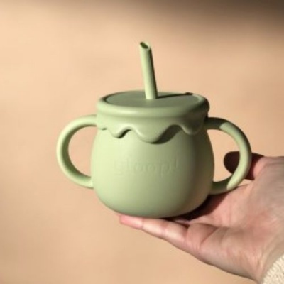 Copo infantil verde claro com tampa e palhinha, segurado por uma mão