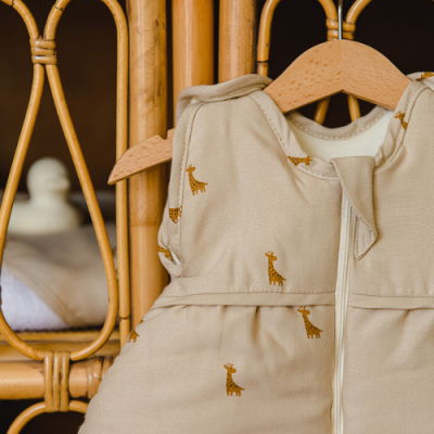 Saco de dormir para bebé bege com padrão de girafas pendurado num cabide de madeira