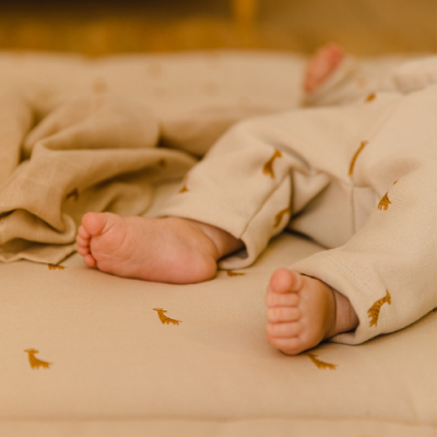 Pés de bebé com calças e colchão bege com padrão de girafas castanhas