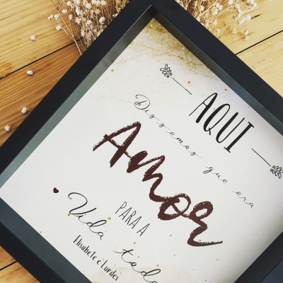 Quadro decorativo com moldura preta e texto em português com flores secas ao fundo.