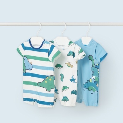 Três macacões curtos com padrões de dinossauros pendurados em cabides brancos