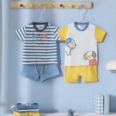 Conjuntos de roupa infantil azul e amarela pendurados numa parede listrada azul.