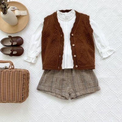 Conjunto infantil com camisa branca, colete castanho, calções cinzentos, sapatos castanhos, chapéu bege e mala de verga