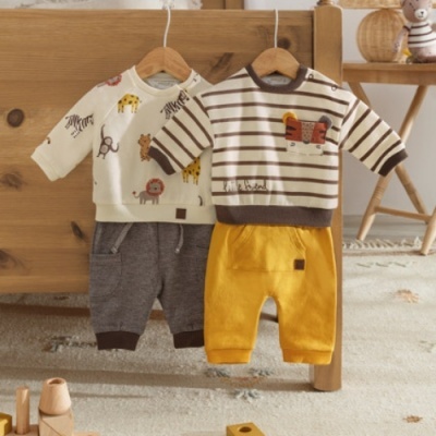 Dois conjuntos de roupa de bebê pendurados com camisolas e calças coloridas em cabides de madeira