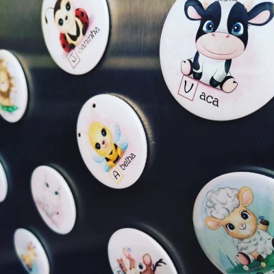 Imãs redondos ilustrados com animais e palavras em português numa superfície metálica