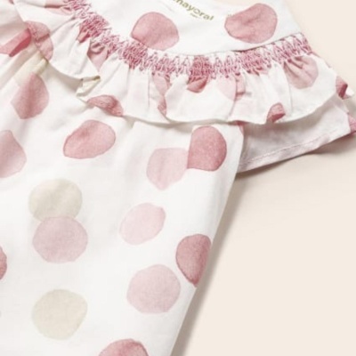 Peça de roupa infantil com padrão de bolas rosa e bege, folhos e costura franzida cor-de-rosa