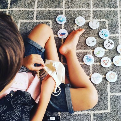 Criança sentada no tapete com bolsa de tecido e marcadores redondos ilustrados