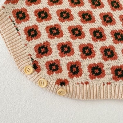 Peça de malha bege com padrão de flores vermelhas e pretas e botões bege na bainha.